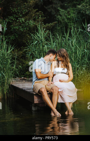 Il marito baci a sua moglie il ventre durante i momenti di relax al lago Foto Stock