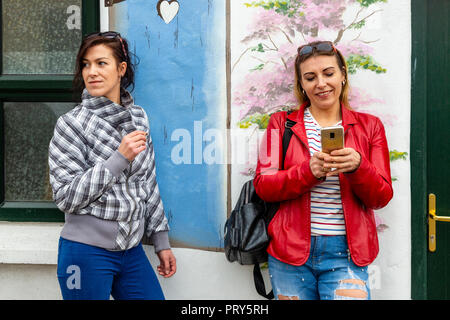 Due donne fumatori e utilizza lo smartphone su strada Foto Stock