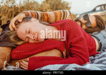 Un hipster paio di donna bionda e bruna uomo con capelli lunghi è agghiacciante e abbracciando sulla coperta in golden sunrise. Foto Stock