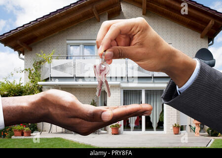 Close-up di agente immobiliare che dà la chiave per Client nella parte anteriore della casa Foto Stock