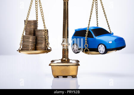 Golden giustizia scala mostrante equilibrio tra monete impilate e auto su sfondo bianco Foto Stock