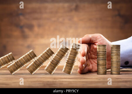 Close-up di un imprenditore la mano proteggere le monete impilate di cadere sulla scrivania in legno Foto Stock