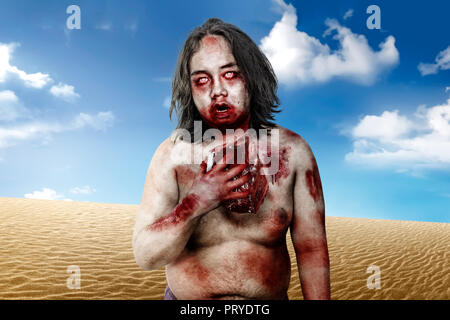 Spooky zombie uomo con bocca sanguinosa tenendo la carne cruda su deserto Foto Stock