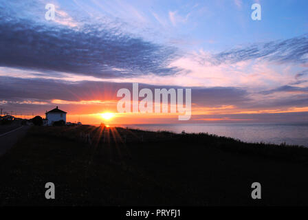 Blu, rosa e arancio Nuvoloso Tramonto in Gaspésie penisola del Quebec, Canada, mostrando una collina nera con una casa locale in contrasto e il mare calmo Foto Stock