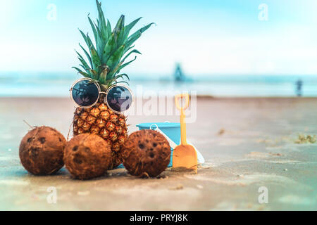 Carino ananas indossando occhiali da sole e noci di cocco rilassante sulla spiaggia Sunny Beach Foto Stock