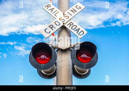 Ruggine vecchia ferrovia segno di incrocio con il semaforo rosso contro il cielo blu con poche nuvole. Foto Stock