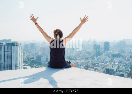 Uomo seduto sul tetto nero e mostra fino a mano con cielo blu di sfondo e sunshine,combattimenti uomo sul tetto Foto Stock