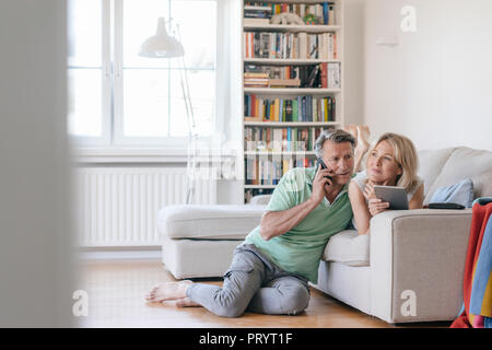 Coppia matura a casa utilizzando il telefono cellulare e PC tablet Foto Stock