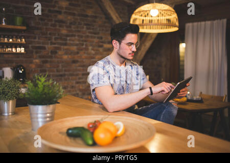 Giovane uomo utilizzando tablet in cucina a casa Foto Stock