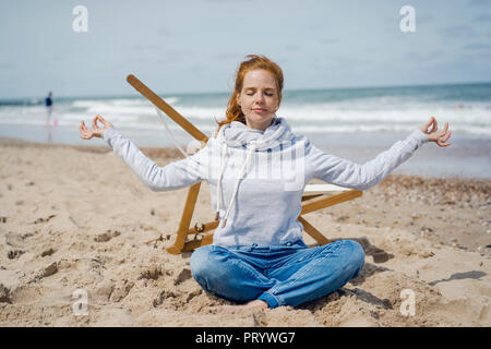 Donna seduta con le gambe incrociate sulla sabbia, meditando sulla spiaggia Foto Stock