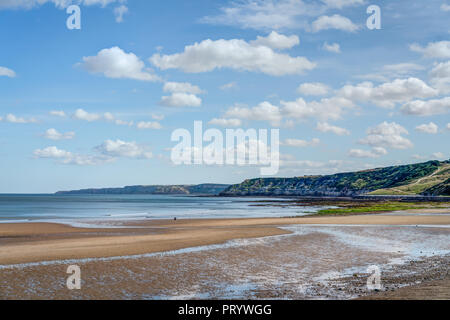 All'estremità sud della spiaggia di sabbia a Scarborough holiday resort guardando giù le scogliere rocciose a Filey Brigg nella distanza. Bella giornata di sole Foto Stock