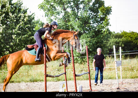 Giovani femmine jockey a cavallo saltando su ostacolo Foto Stock