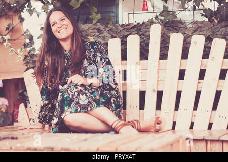 Hippy stile di vestiti e capelli lady come '70s seduto su una panca di legno ha reso il mio materiali riciclati luce esterna e rilassata lady in attività del tempo libero outsid Foto Stock