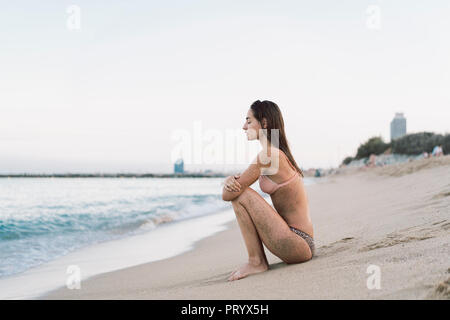 Bella donna seduta sulla spiaggia con gli occhi chiusi Foto Stock