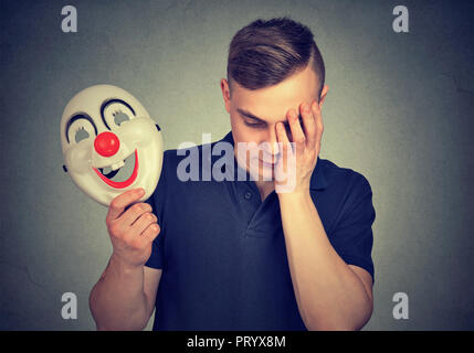 Giovane Azienda colorata maschera clown e guardando sconvolto essendo in depressione e nascondere i sentimenti Foto Stock