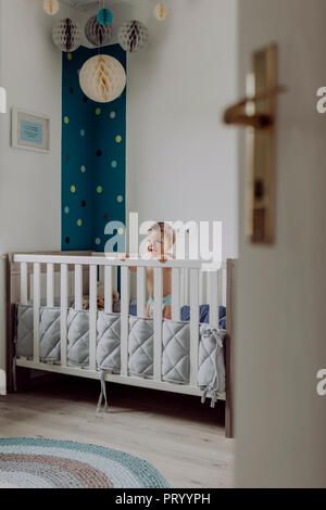 Baby boy in piedi nella sua culla, ridendo Foto Stock