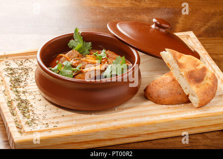 Tjvjik - fegato di agnello, cuore e polmoni stufati con cipolla e pomodoro -. Cucina armena tradizionale servita su tavola di legno su una pentola di argilla. Foto Stock