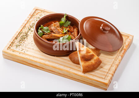 Tjvjik - fegato di agnello, cuore e polmoni stufati con cipolla e pomodoro -. Cucina armena tradizionale servita su tavola di legno su una pentola di argilla. Foto Stock