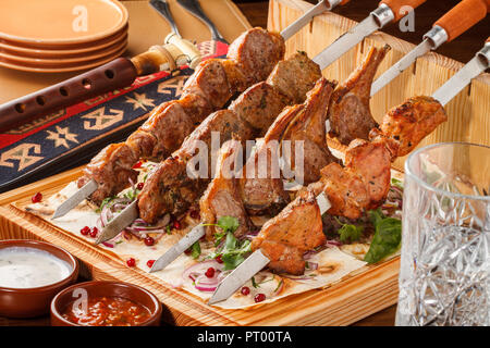 Khorovats- piatto tradizionale armeno Kebab/spiedini su tavola di legno. Spiedini di vitello, agnello, maiale e pollo serviti su pane piatto. Foto Stock