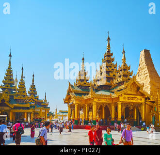 YANGON, MYANMAR - Febbraio 27, 2018: i visitatori di Shwedagon pagoda a piedi lungo l'immagine ornati case con pyatthat (multilivello) tetti, medievale s Foto Stock