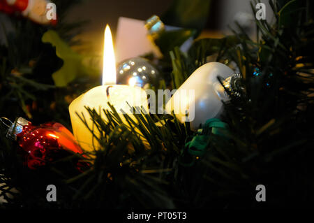 Singola Lit candela accoccolato sul ramo di un natale abete circondato da rosso e bianco baubles. Foto Stock