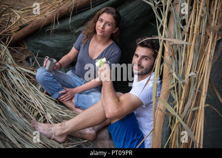Matura in amore viaggiare e trascorrere del tempo insieme in paglia tenda mentre bevendo un tè caldo dal fiume Foto Stock