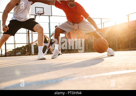 Immagine ritagliata di giovani uomini multietnica i giocatori di basket giocare a basket al campo sportivo Foto Stock