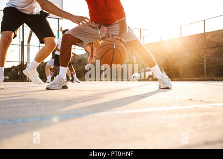 Immagine ritagliata di forti uomini multietnica i giocatori di basket giocare a basket al campo sportivo Foto Stock