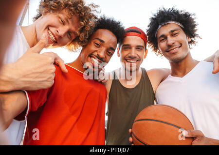 Giovane bella ragazzi sorridenti e tenendo selfie mentre giocare a basket al parco giochi all'aperto durante il periodo estivo giornata di sole Foto Stock