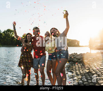 Coriandoli intorno al gruppo di felice amici divertendosi in un fiume al tramonto Foto Stock