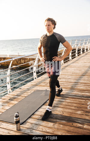 Ritratto di un concentrato di uno sportivo facendo balzi in avanti esercitazioni su un tappetino fitness spiaggia, ascoltando la musica con gli auricolari Foto Stock