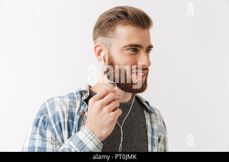 Ritratto di un sorridente giovane uomo barbuto in piedi isolato su bianco, parlando tramite auricolari Foto Stock