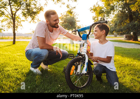 Giovane padre e suo figlio per divertirsi insieme al green park, fissaggio insieme per bicicletta Foto Stock