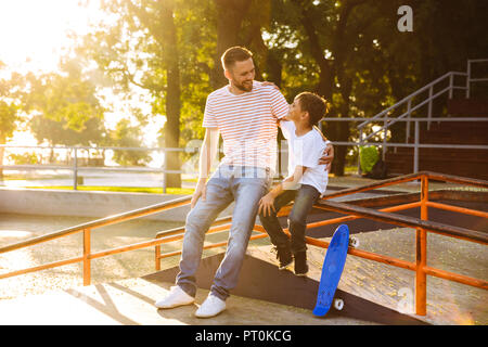 Padre sorridente di trascorrere del tempo con il suo piccolo figlio a skate park, avvolgente Foto Stock