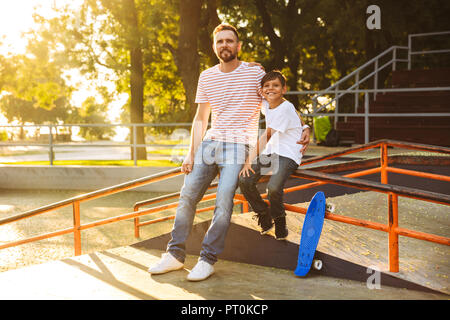 Padre felice di trascorrere del tempo con il suo piccolo figlio a skate park, avvolgente Foto Stock