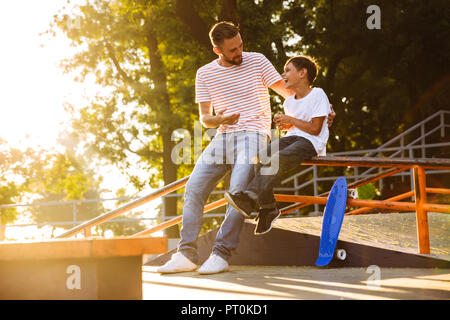 Ridendo padre di trascorrere del tempo con il suo piccolo figlio a skate park, avvolgente Foto Stock