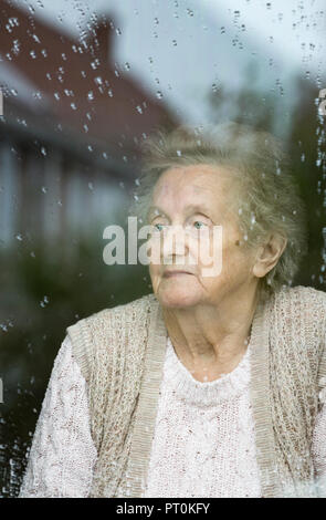 Donna di novanta anni che guarda fuori dalla finestra in un giorno di pioggia. Autoisolamento, quarantena, Coronavirus, concetto di distanza sociale... Foto Stock