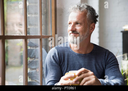 Mture uomo prendendo una pausa, bere il caffè alla finestra del suo appartamento loft Foto Stock