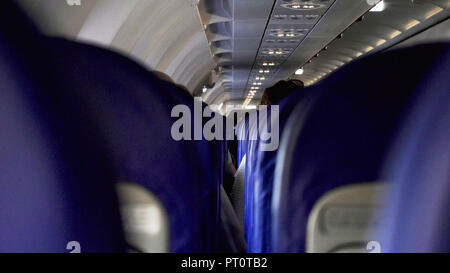 Candid shot tra i sedili dei passeggeri seduti all'interno aereo mentre si è in viaggio. Foto Stock