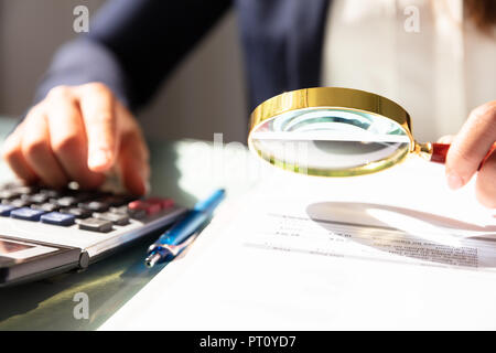 Close-up di una imprenditrice la mano esaminando fattura attraverso la lente di ingrandimento Foto Stock