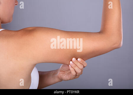 Close-up di una donna tenendo il braccio con un eccesso di grasso su sfondo grigio Foto Stock