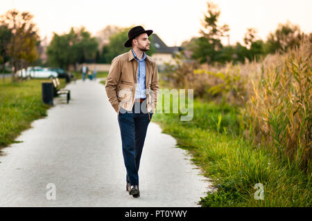 Bello ed elegante uomo nel parco indossare giacca e fedora hat. Foto Stock