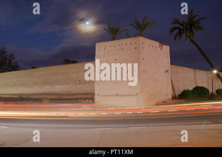 Notte skyline di Marrakech parete storiche che circondano la città vecchia (medina), marciapiede, sky con la luna, palme, auto luci, lunga esposizione, senza le persone. Foto Stock