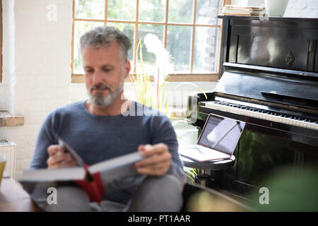 Portatile su uno sgabello davanti al pianoforte, uomo lettura nel libro Foto Stock