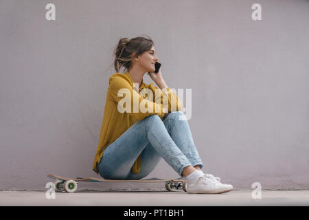 Giovane donna seduta su skateboard, utilizza lo smartphone Foto Stock