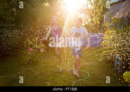 Fratello e Sorella e divertirsi con sprinkler prato in giardino Foto Stock