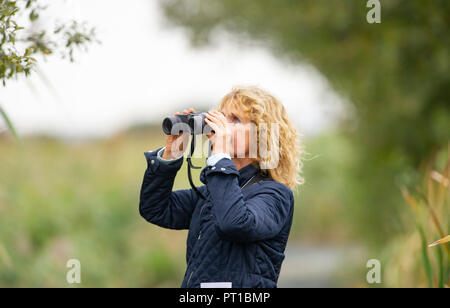 Rainham Marshes Essex REGNO UNITO - donna matura di mezza età birdwatching con il binocolo Foto Stock