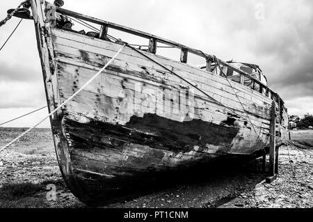 Il vecchio tradizionale in legno scafo della nave che mostra usura eccessiva e di abbandono puntellato e legato al fine di impedire che cada su come il legato si alza e si abbassa. Foto Stock