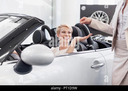 Presso il rivenditore di auto, donna nel convertibile ricevere le chiavi dell'auto Foto Stock