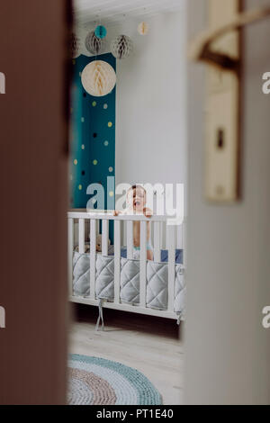 Baby boy in piedi nella sua culla, ridendo Foto Stock